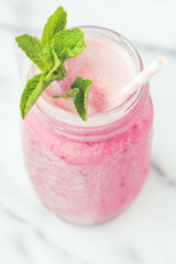 Fruit pink smoothie in a glass jar on a white marble. Minimalist style. Trend vintage toned.