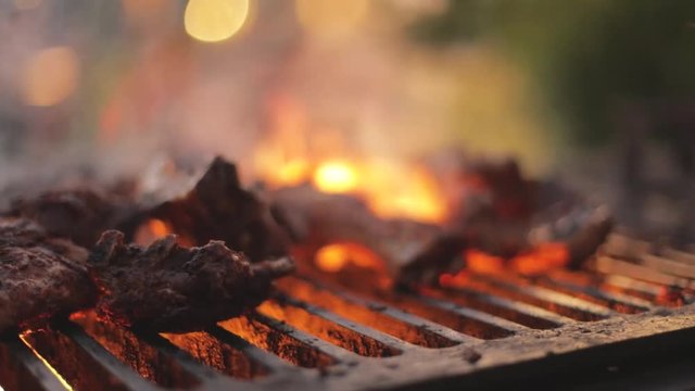 People barbecuing ribs over an open flame on a beautiful summer evening.