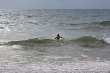 Phuket, Thailand. Thai child swims on the wave in the Andaman sea to surf. View from Karon beach