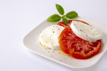 Fototapeta na wymiar Mozzarella and tomatoes with basil on a white square plate. The background is white. Copiespice.