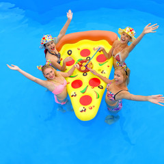 Four young girls wearing bikinis gather around  an inflatable sun bed with a large cocktail drink  placed in the middle of them.They laugh and joke  together having fun in a swimming pool.