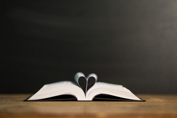 Naklejka premium Book page in heart shape with dark background. Conceptual Heart from Book. Copy Space