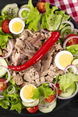 Salad with tuna, anchovies and vegetables. Mediterranean food. The background is black. Top view. Copy space. Vertical shot.