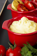 Food is still life. Two red pots with potato puree and fried vegetables on a black tray. Background black marble.