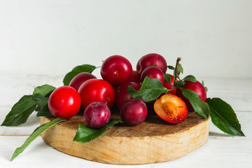 Fresh red plum with leaves on a wooden light background