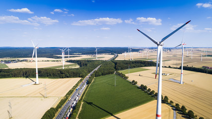 Aerial view of windmill against blue sky with clouds. Wind turbine farm and a road between agricultural fields.