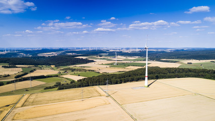 Fototapeta na wymiar Aerial view of windmill against blue sky with clouds. Wind turbine farm and a road between agricultural fields.