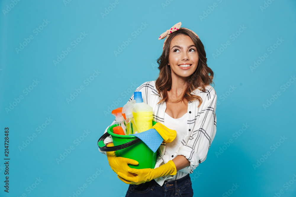 Poster Image of european woman 20s wearing yellow rubber gloves for hands protection holding bucket with detergents, isolated over blue background