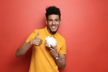 African-American man with piggy bank on color background