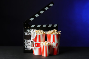Buckets with tasty popcorn and movie clapper on dark background