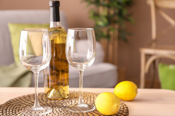 Wooden table with glasses, bottle of wine and lemons in living room