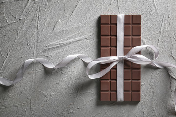 Tasty milk chocolate bar with ribbon on textured background