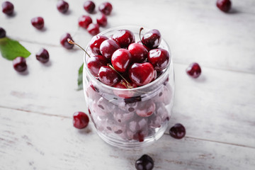Glass with tasty ripe cherries on white wooden background