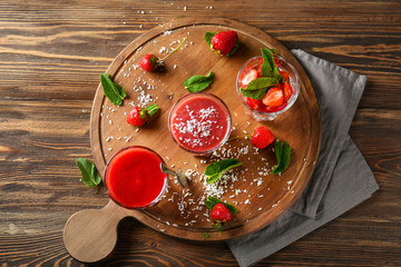 Wooden board with glasses of strawberry smoothies on table
