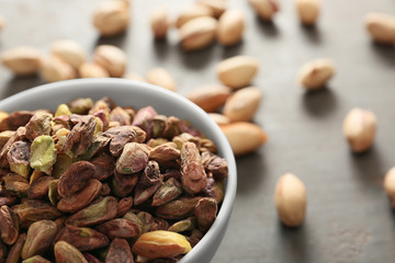 Bowl with tasty pistachio nuts on table, closeup