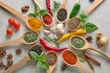 Wooden spoons with different spices on grey background