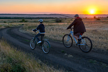 Fototapeta na wymiar father and son ride a bike in the evening field 