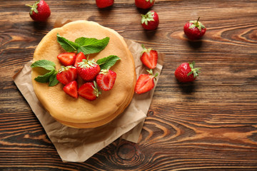 Delicious pancakes and strawberries on wooden table