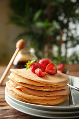 Plate with delicious pancakes and strawberries on wooden table
