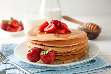 Delicious pancakes with strawberries and honey on table