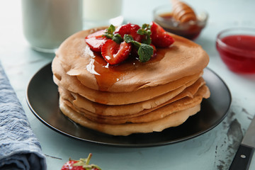 Plate with delicious pancakes, honey and strawberries on table