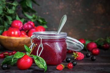 assortment of jam in glass jars, seasonal fresh berries and fruit plum, strawberry, currant, raspberries on a dark background selective focus with copy space, crop concept