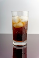 Cola and ice cubes in glass on white background with selective focus and crop fragment