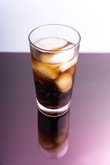 Cola and ice cubes in glass on white background with selective focus and crop fragment