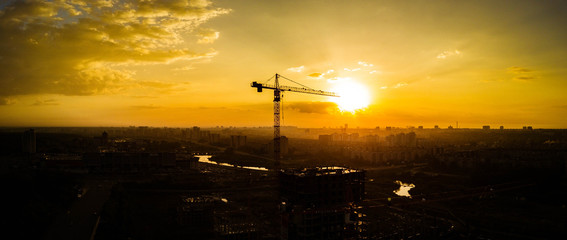 Panoramic photo of silhouette of construction crane on the background of the warm evening sun, construction of a new district, Chelyabinsk, Russia