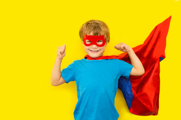 Cute smiling child boy in Superhero costume  showing his biceps on a yellow background.