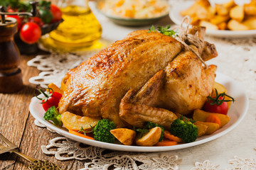 Roast chicken whole. Served on a plate with vegetables and baked potatoes.