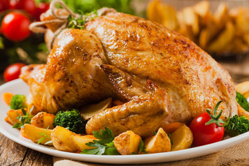 Roast chicken whole. Served on a plate with vegetables and baked potatoes.