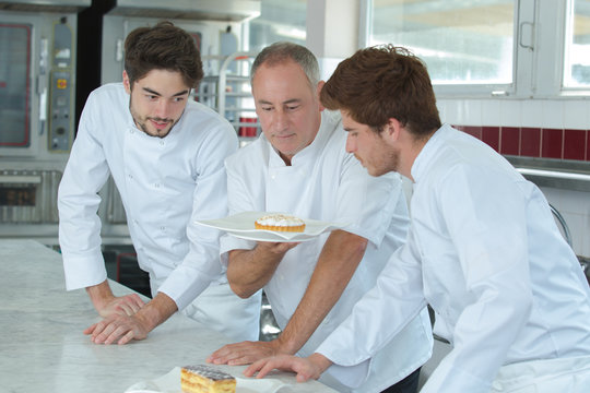 young assistants and mature chef looking at finished cake