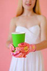 Woman wearing gloves keeping green glass with tea in pink monophonic background. Concept of drinks...