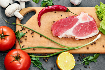 Fresh beef steak, wooden spoon, Assortment of Fresh Vegetables, aromatic herbs, spices and vegetables for cooking , on black  background, top view. Meat