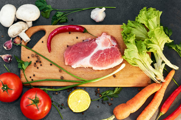 Fresh beef steak, wooden spoon, Assortment of Fresh Vegetables, aromatic herbs, spices and vegetables for cooking , on black  background, top view. Meat