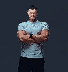 Portrait of a muscular handsome bodybuilder in sportswear, standing with crossed arms in a studio.