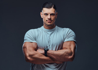 Portrait of a muscular handsome bodybuilder in sportswear, standing with crossed arms in a studio.