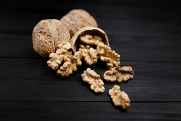 Walnut and walnut kernels and whole walnuts on rustic black wooden background.