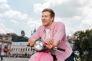 City atmosphere. Exuberant cheerful man posing on motorbike and laughing