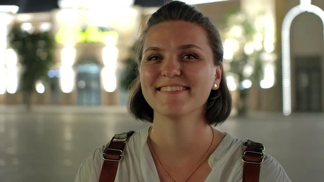 A close-up shot of a pretty young woman smiling with a shining amusement park and the glowing carrousel on the background