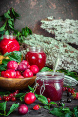 assortment of jam in glass jars, seasonal fresh berries and fruit plum, strawberry, currant, raspberries on a dark background selective focus with copy space, crop concept