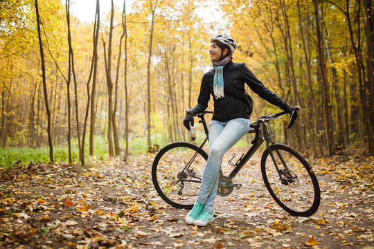 Picture of girl in helmet, jeans next to bicycle in autumn park