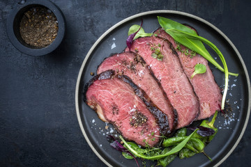 Traditional barbecue aged sliced fillet steak with wild garlic and fruits top view on a plate with copy space