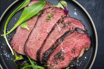 Traditionelles Barbecue Filet Steak aufgeschnitten mit Bärlauch und Früchten als Draufsicht auf einem Teller