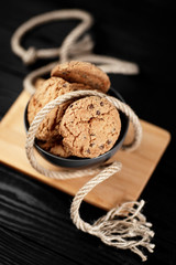 Delicious chocolate cookies in a dish on the wood black background decorated with a rope.