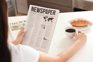 Young woman reading newspaper while drinking coffee in kitchen