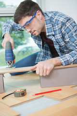 young male carpenter cutting wooden plank with bandsaw in workshop