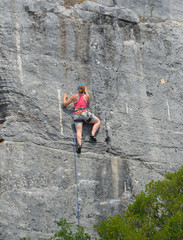 Woman in red top Rock Climbing on Rock Face.