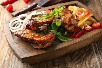 Wooden board with delicious grilled ribs and french fries on table